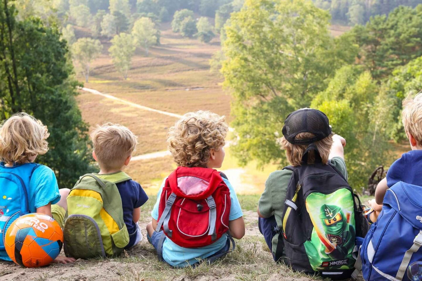 Gruppe von Kindern sitzt auf dem Boden und schaut auf die weitläufige Heidelandschaft in der Fischbeker Heide.
