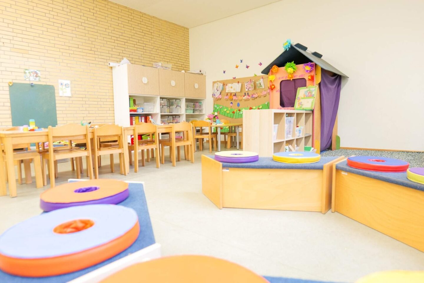 Sitzkreis in einem Gruppenraum der Kita Archenholzstraße mit bunten Kissen und Bodenmatten, perfekt für gemeinsames Lernen, Gruppenspiele und pädagogische Kreisspiele."