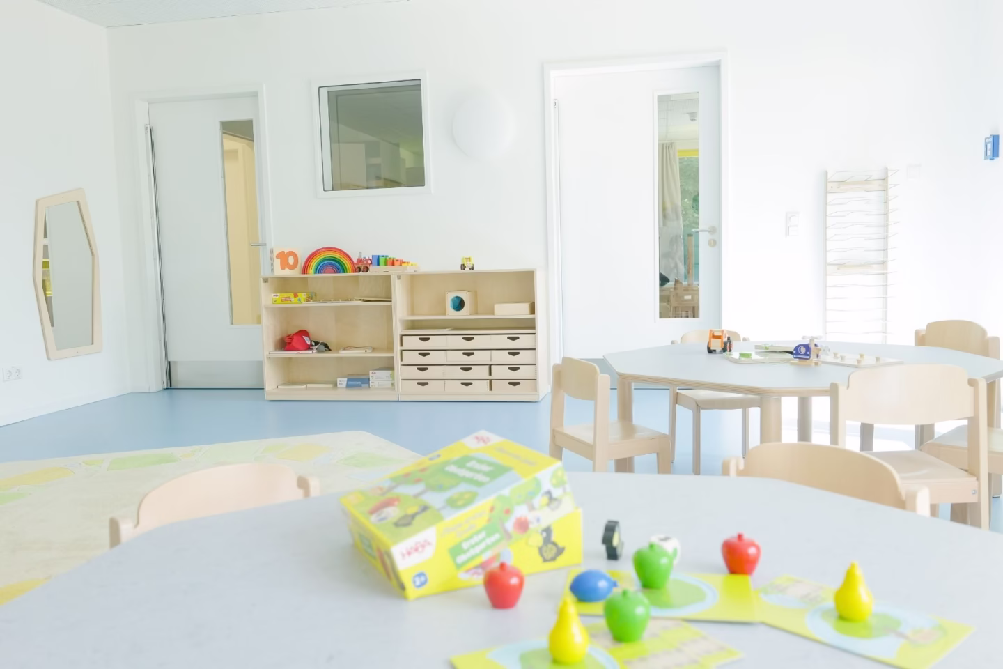 Heller Kita-Gruppenraum mit kindgerechten Tischen, Stühlen und Spielmaterialien
