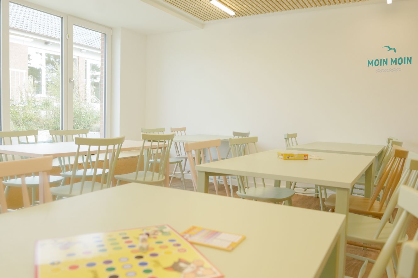 Heller Gruppenraum in unserer Strandperle auf Sylt mit vielen Gruppentischen & -Stühlen und einem Mensch-Ärger-Dich-Nicht-Spiel auf einer Tischgruppe