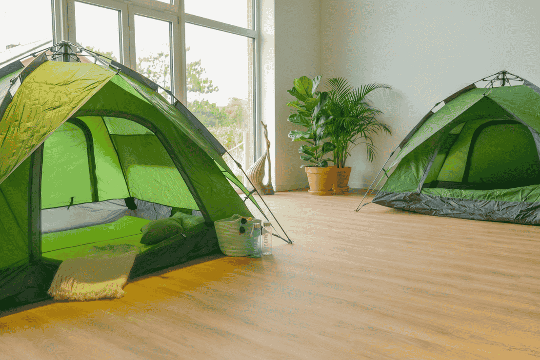 Indoor-Campingraum in unserer Strandperle: zwei grüne Zelte aufgestellt in einem Raum, große Fensterfront und einer Grünpflanze im Hintrergrund